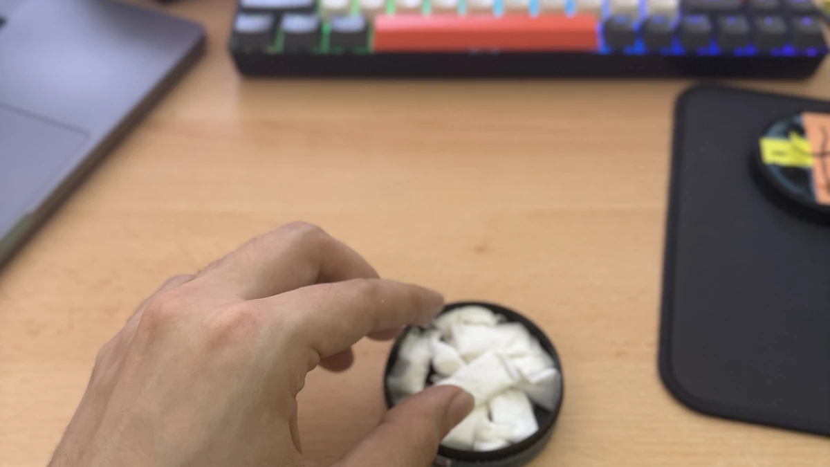 Griff in eine offene Snus-Dose am Schreibtisch